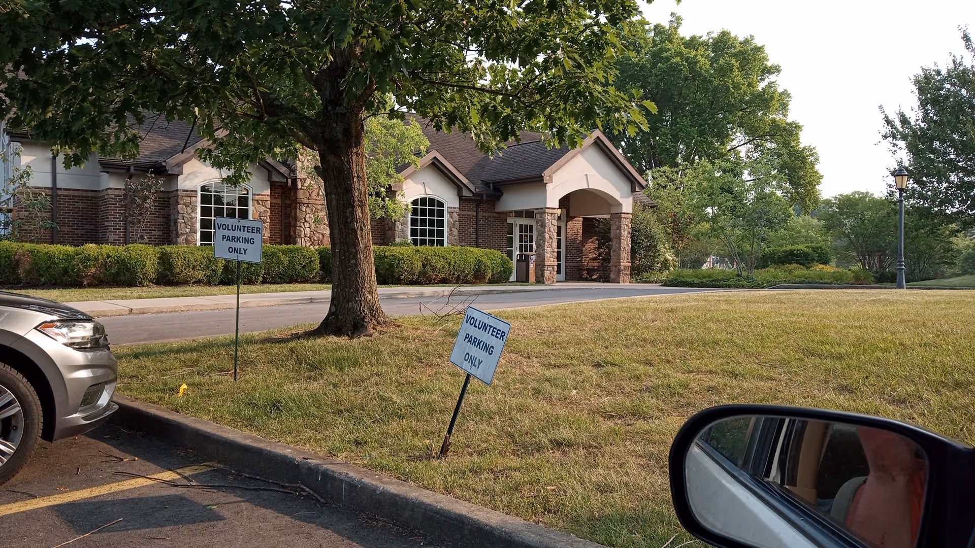 Exterior view of a brick hospice-style building with arched entrance and surrounding parking.