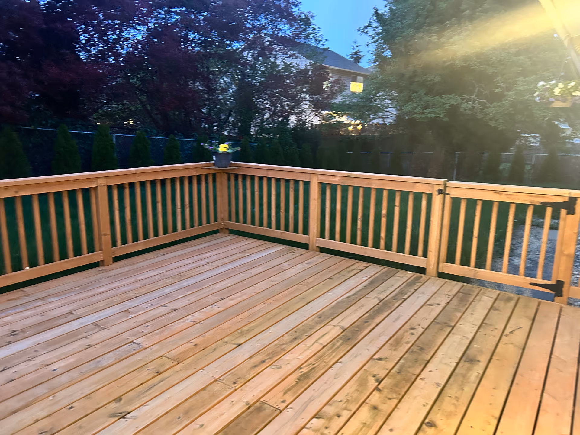 A wooden outdoor deck with railing, a potted plant, and surrounding trees.