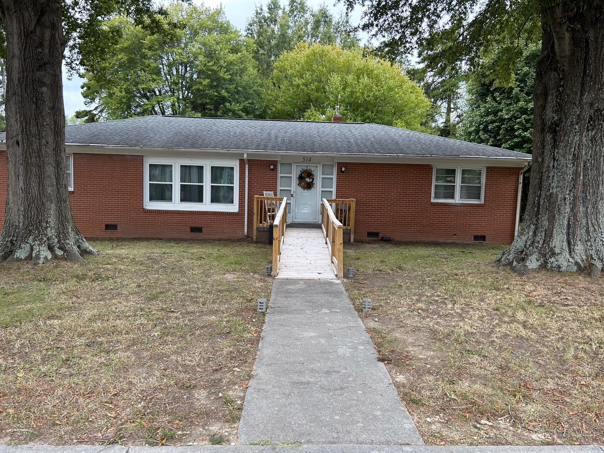 Front exterior of Ginnie Mae Residence Care, a brick, single-story building with a ramp and trees.