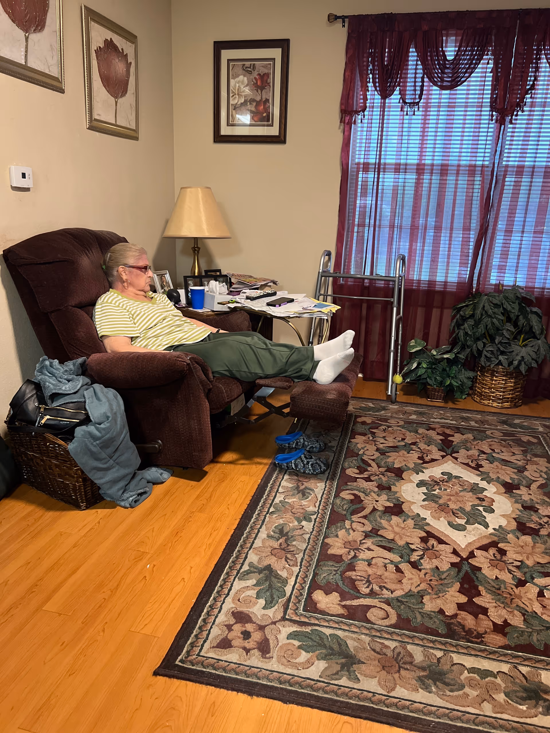An elderly person relaxing in a brown recliner in a living room with a walker nearby.