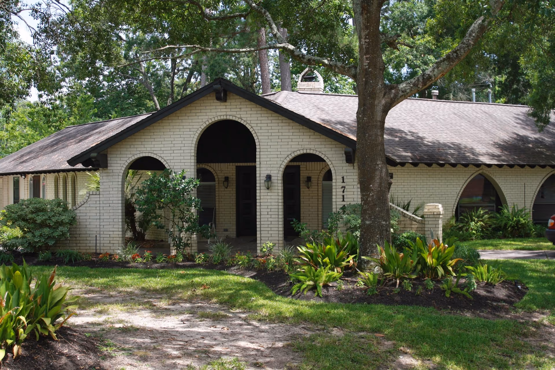 Single-story brick building with arched entrances, landscaped front yard, and large trees.