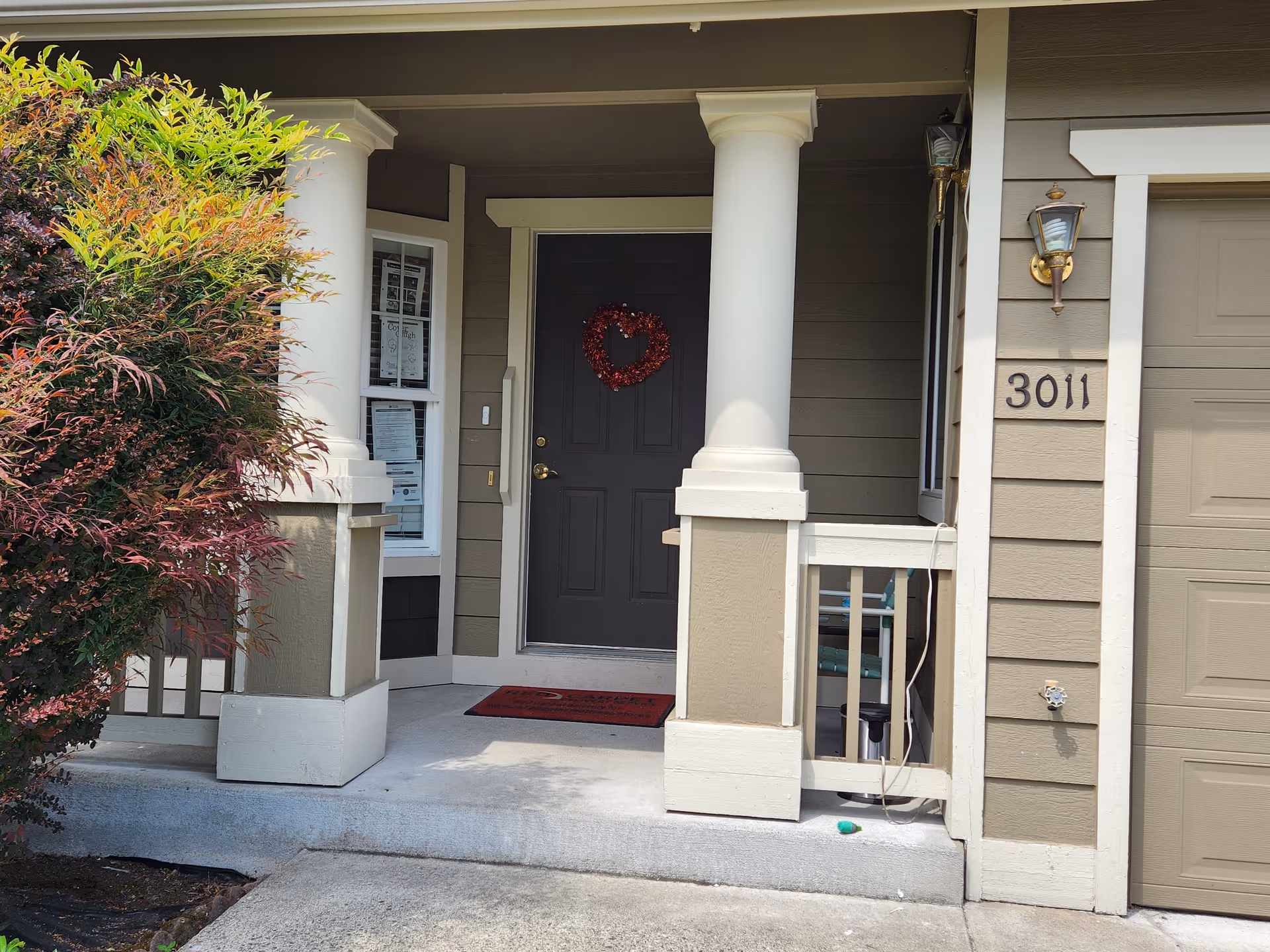Front entrance of Mukilteo Green House, tan building with white columns, wreath, and red doormat.