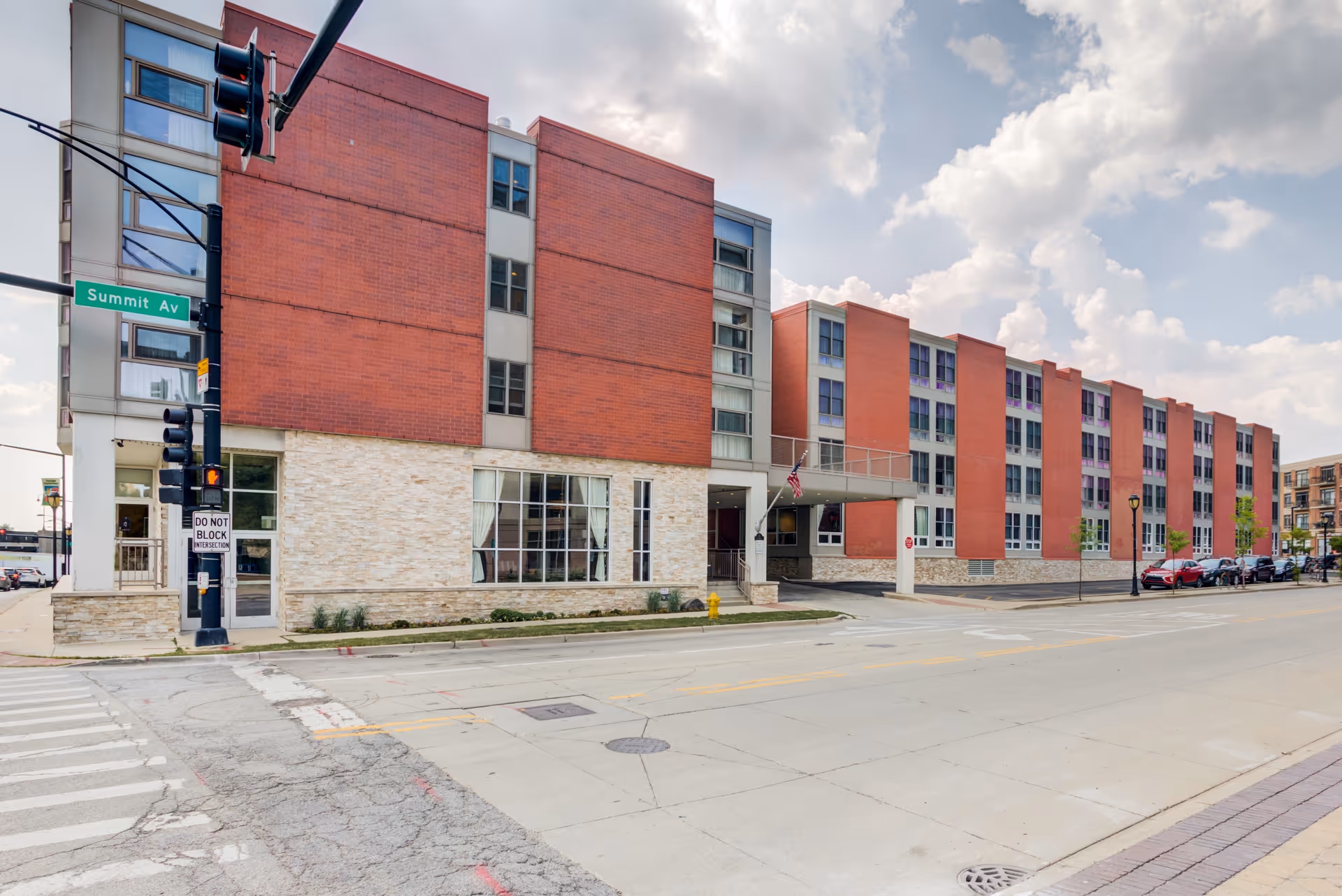 Facade of Summit of Uptown senior living building along a city street, brick and glass.