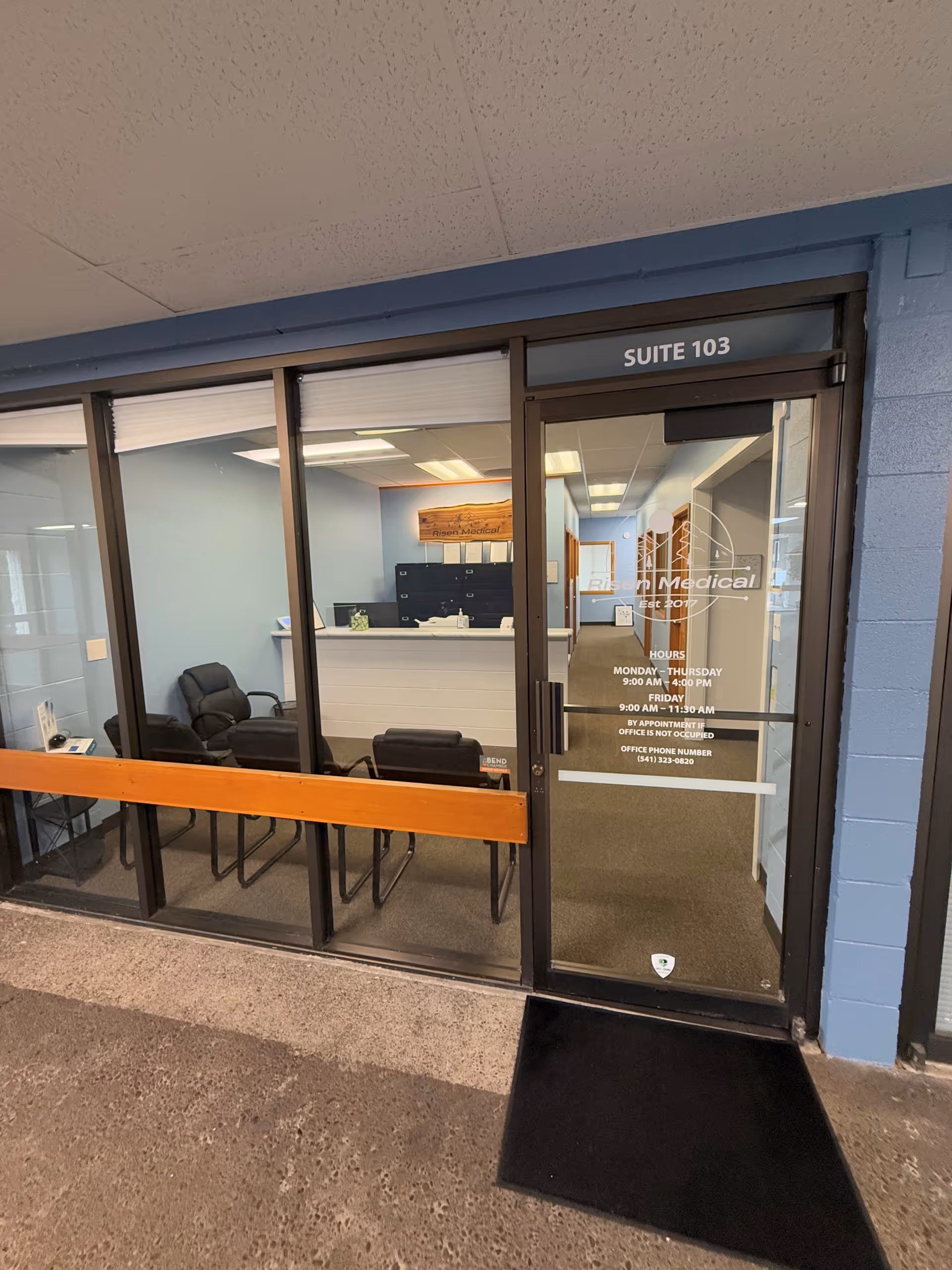Glass-walled reception area inside Risen Medical Bend, showing seating and a Suite 103 door.