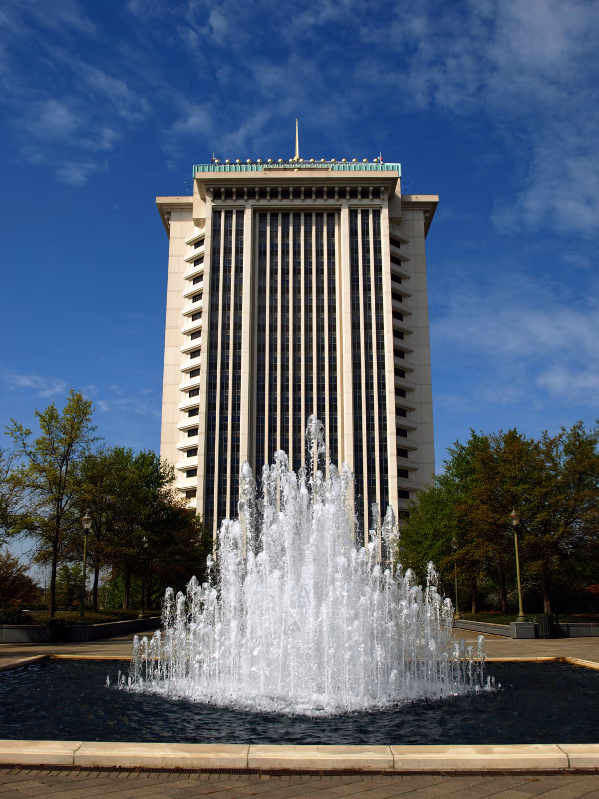 Tall modern building with a large central fountain in a circular basin outdoors.