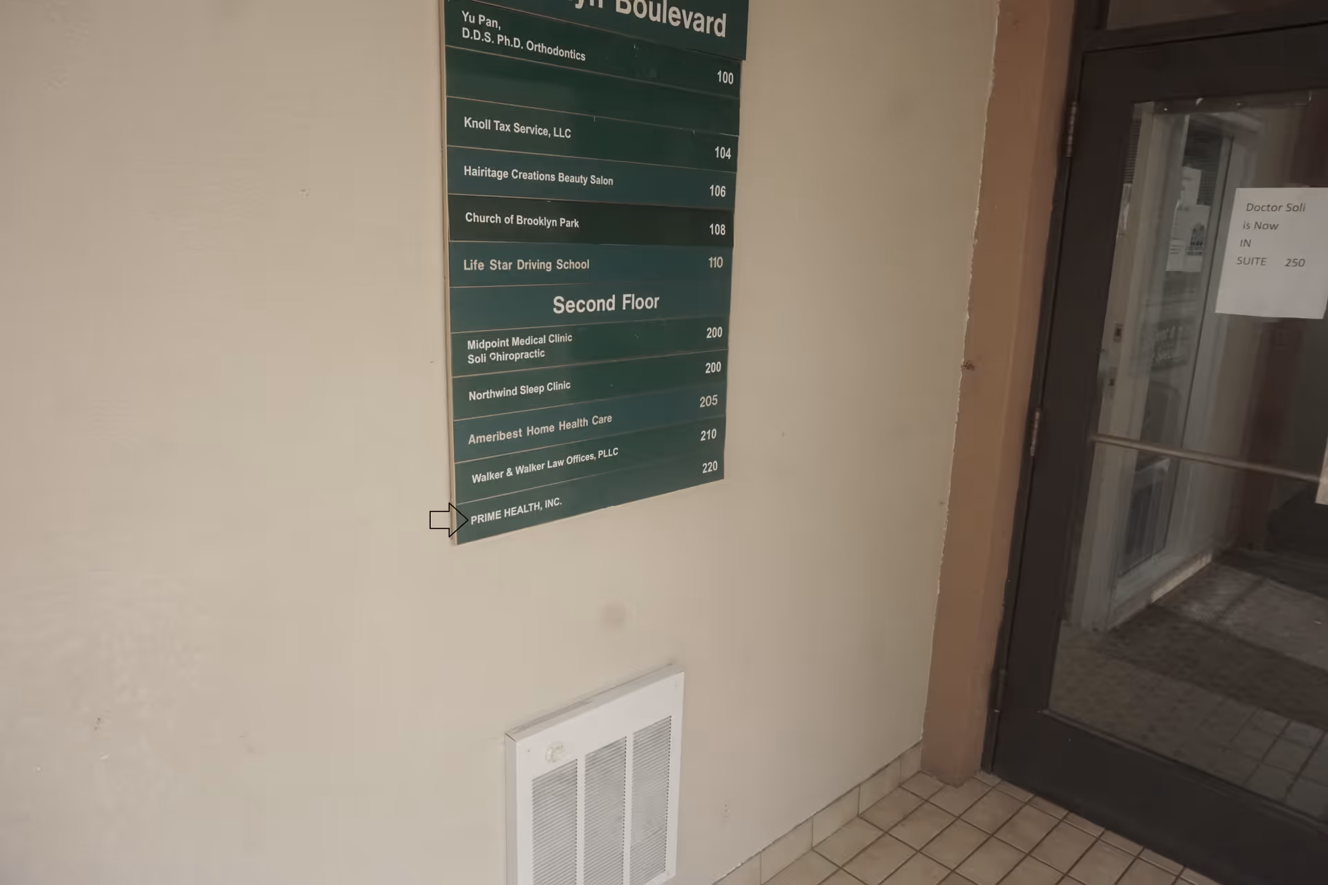 Interior hallway with a green directory sign listing second floor offices and a glass door.