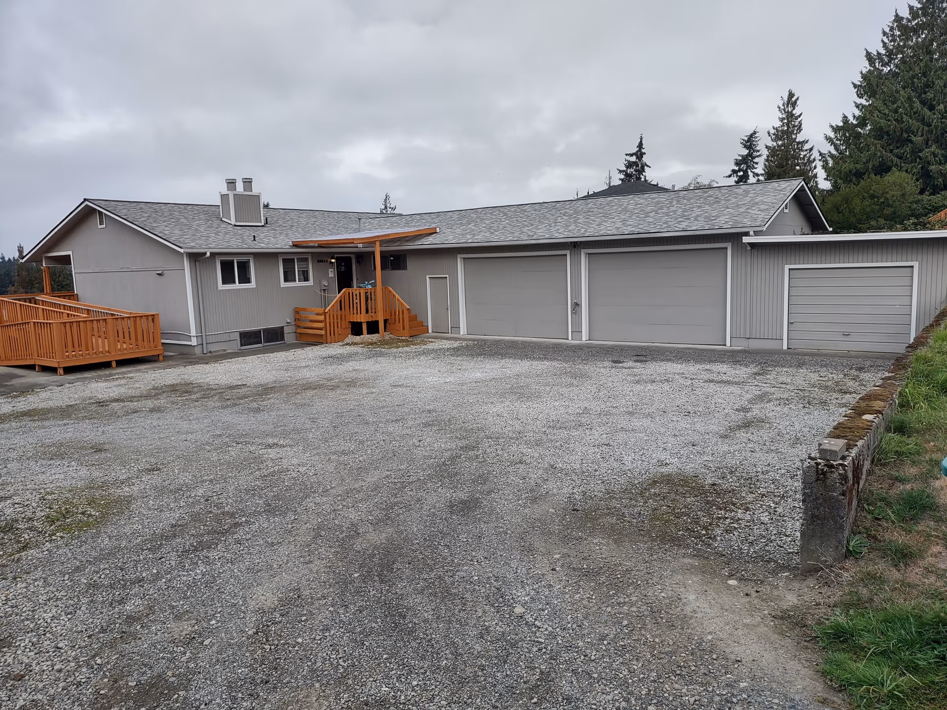 Single-story grey facility with garages, gravel lot, and wooden deck stairs.