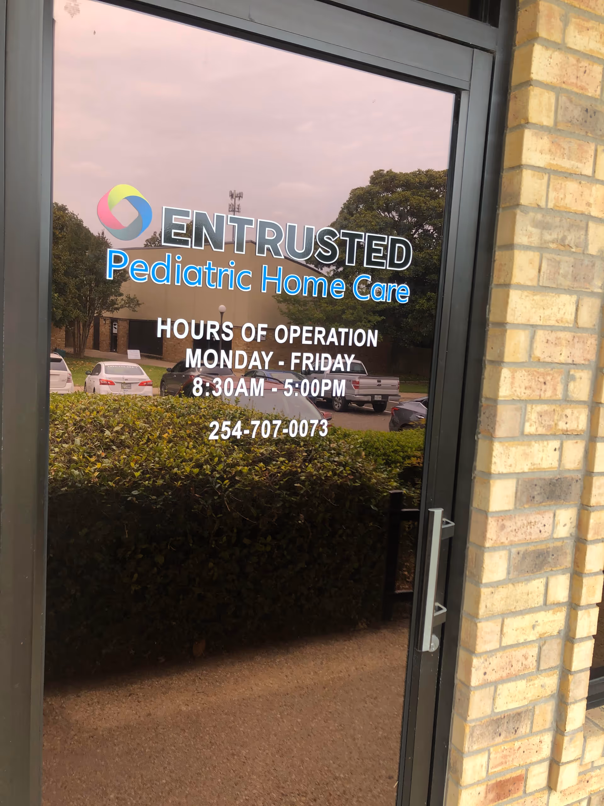 Glass door entry displays Entrusted Pediatric Home Care signage and hours of operation.