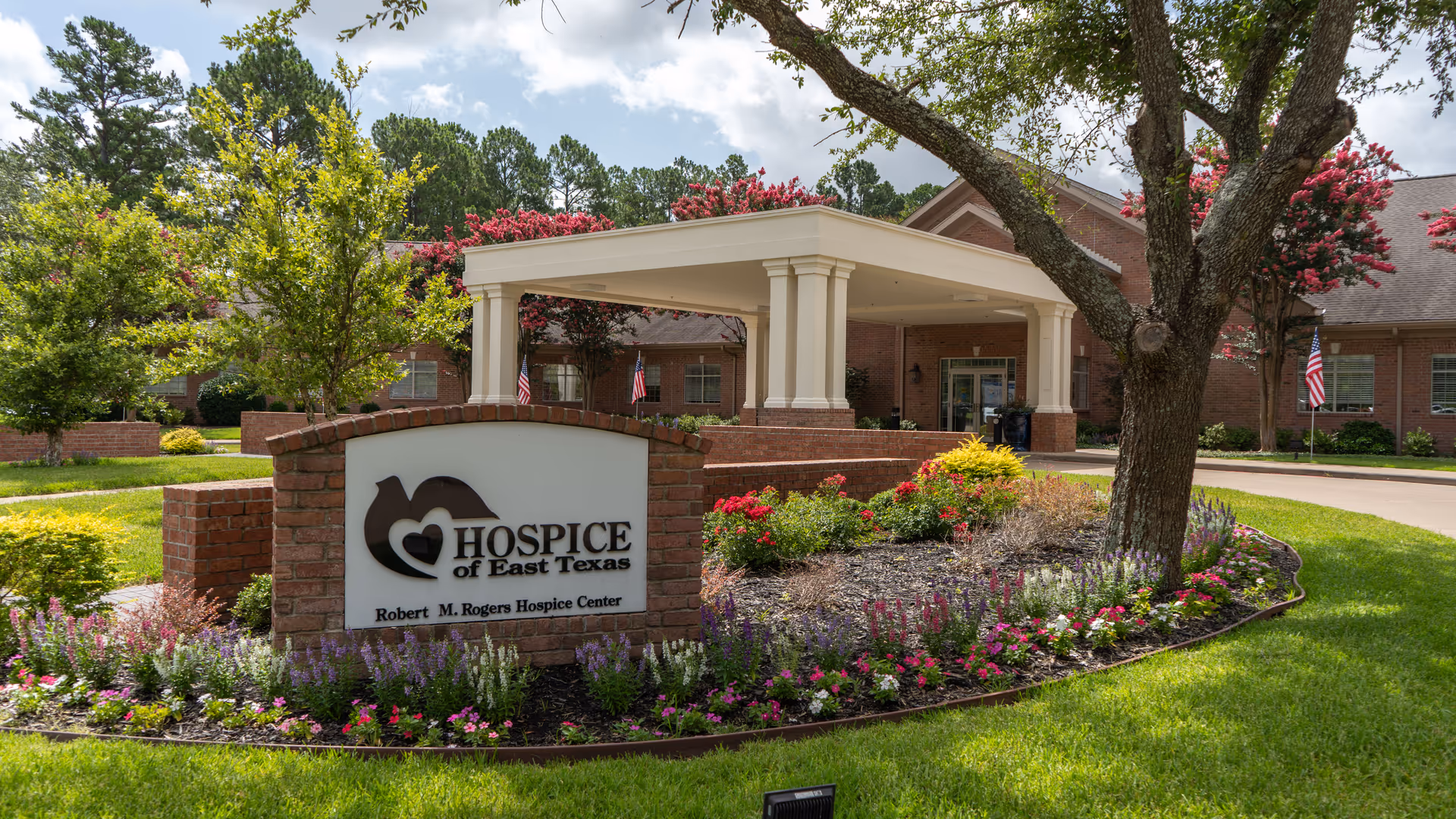 Hospice of East Texas sign sits in a landscaped flower bed by a brick building entrance.