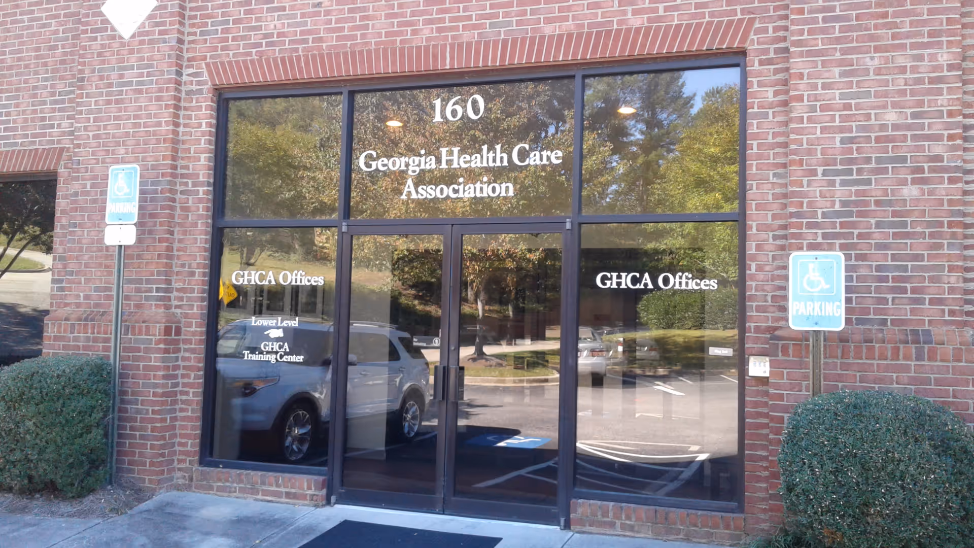 Brick building exterior with glass doors labeled Georgia Health Care Association and handicap parking signs.