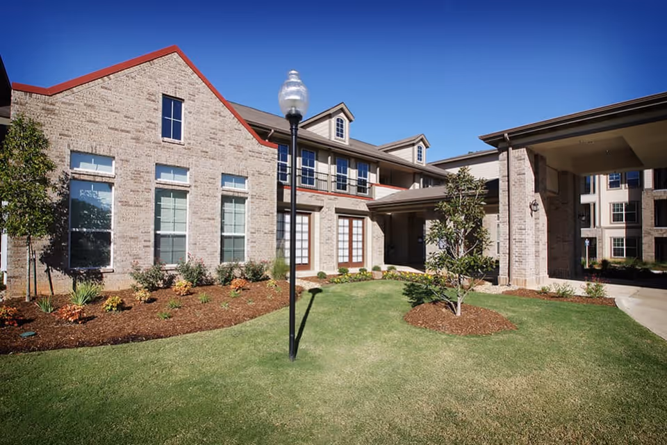 Exterior view of a brick senior living facility with a green lawn.