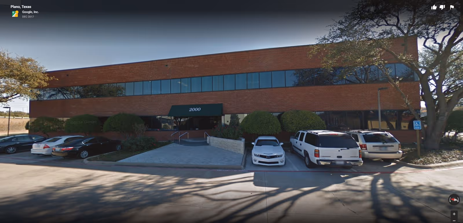 Brick office building with glass windows, entrance canopy, and several parked cars in front.