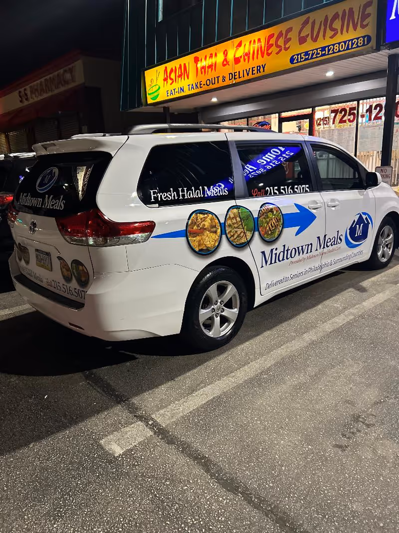 White Midtown Meals van parked on street beside Asian restaurant storefront at night.