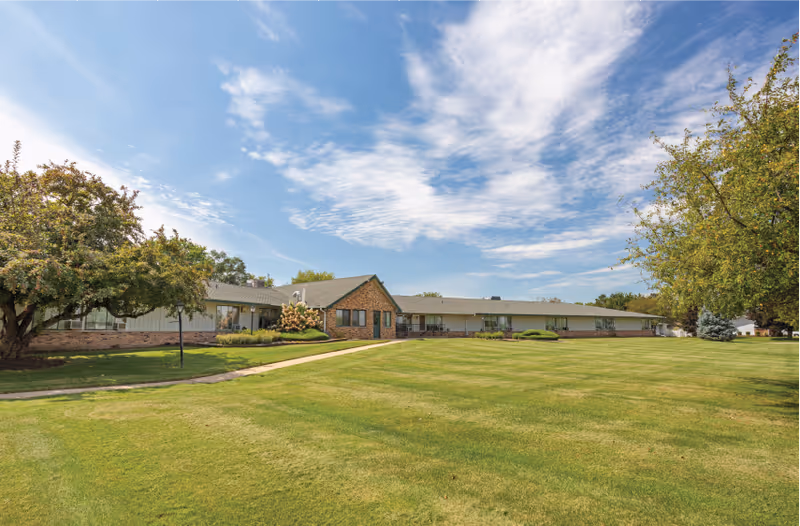 Wide view of a single-story senior care center with a spacious green lawn and blue sky.