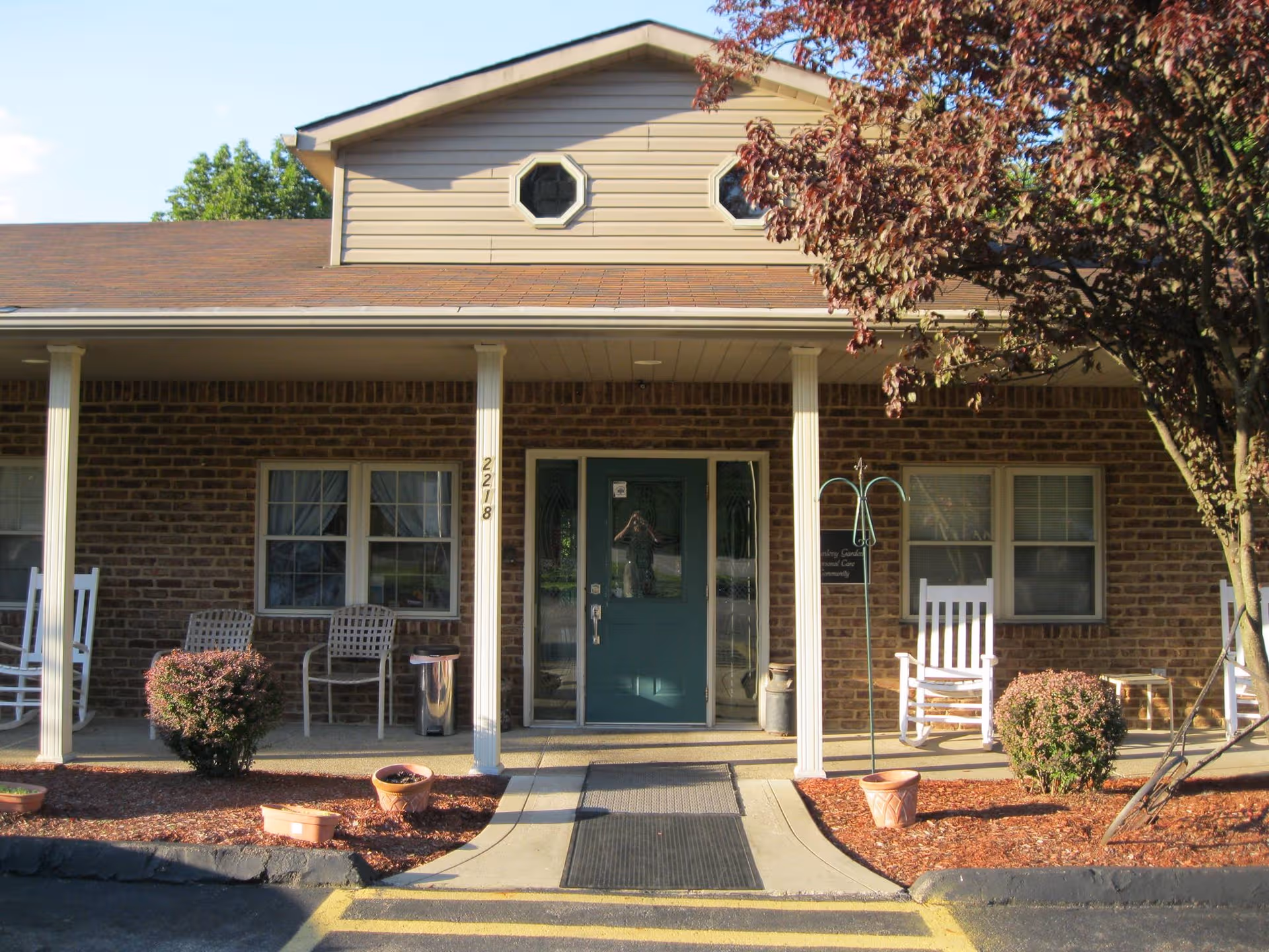 Brick senior care home with a covered porch, rocking chairs, and a teal front door.