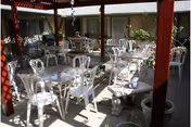 Outdoor covered patio with white plastic tables and chairs arranged for dining.