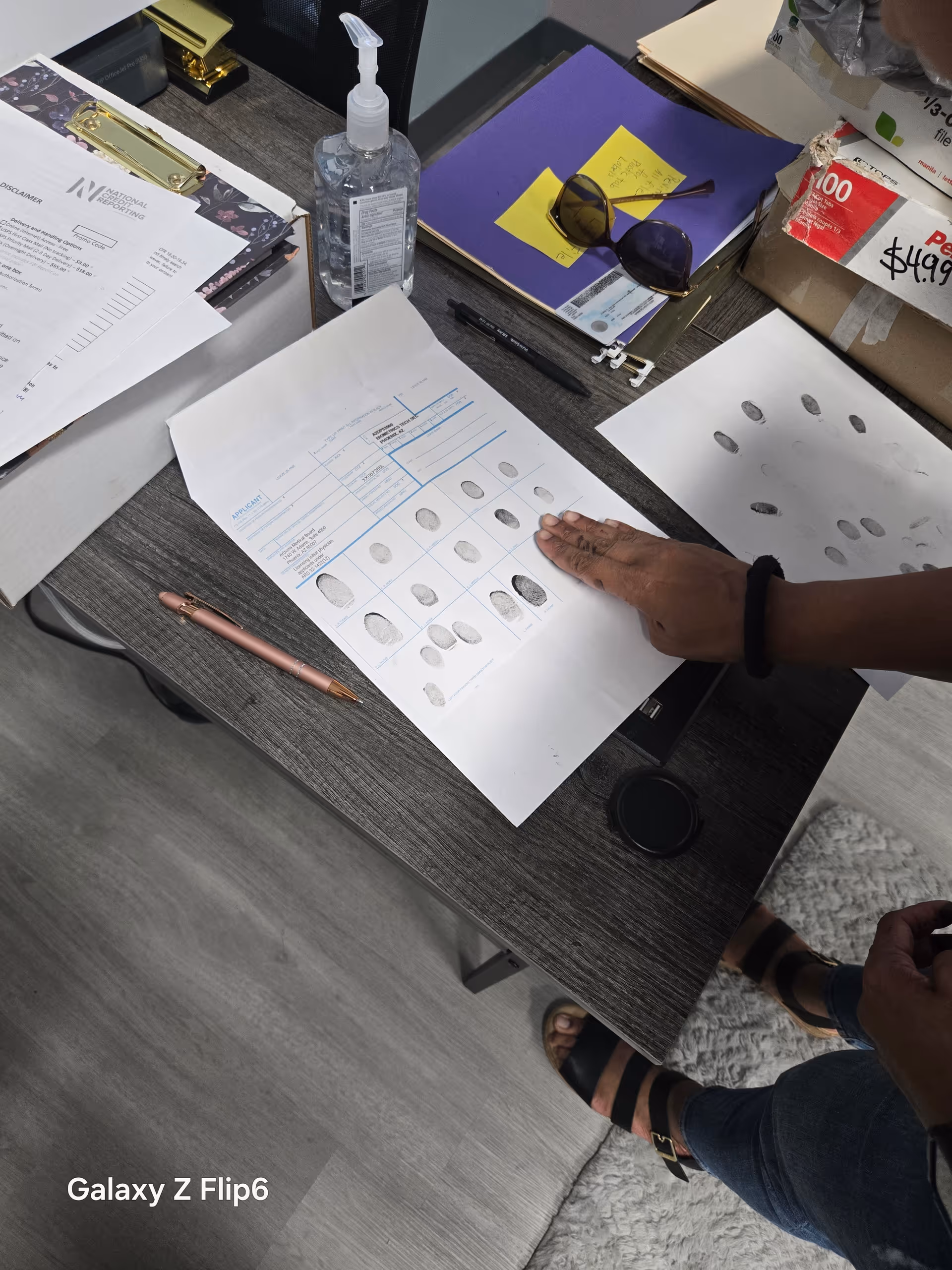 Hand points to fingerprint chart on desk amid papers and office supplies.