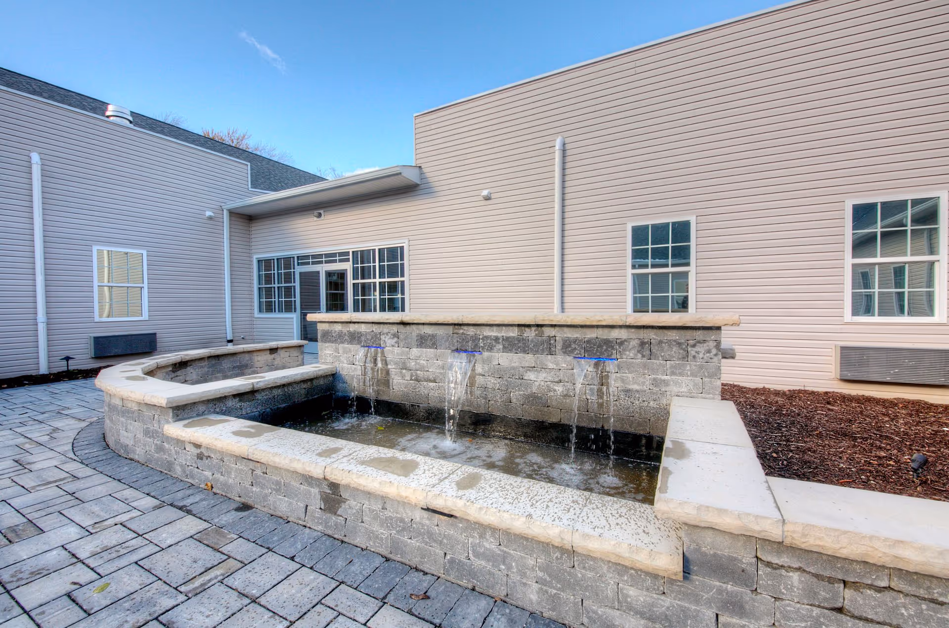 Exterior view of Meadows Assisted Living with a brick fountain and entrance courtyard.