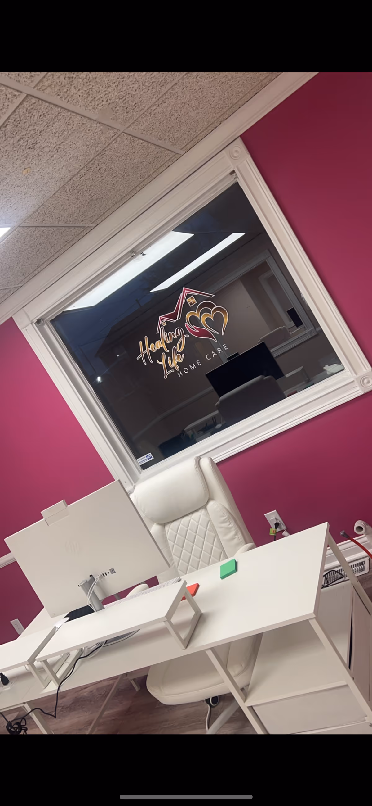 White desk and chair in magenta-walled office with a window displaying Healing Life Home Care logo.