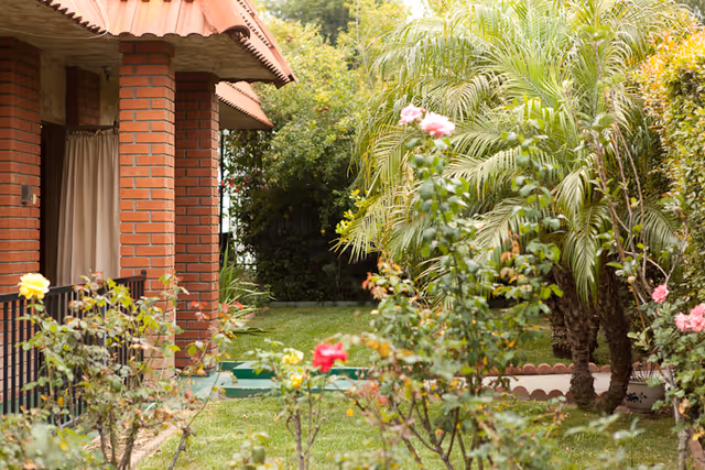 Brick building front with a covered porch and a garden with roses and palm trees