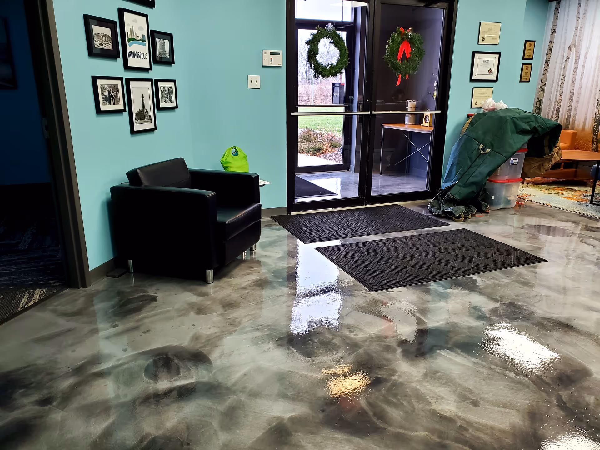 Lobby area with teal walls, framed photos, black chairs, and glass entrance doors.