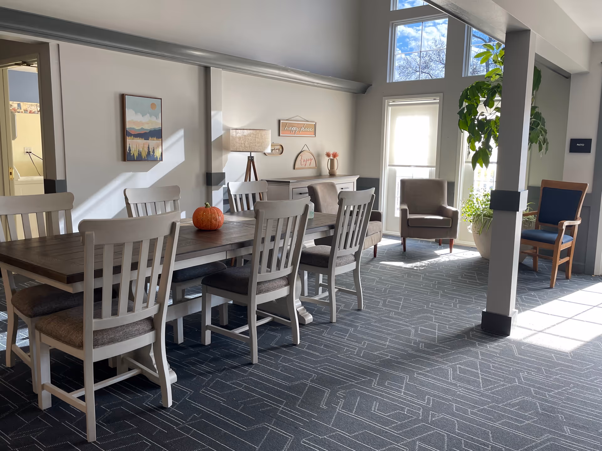 Bright dining area with long wooden table, white chairs, and sunlit lounge seating.