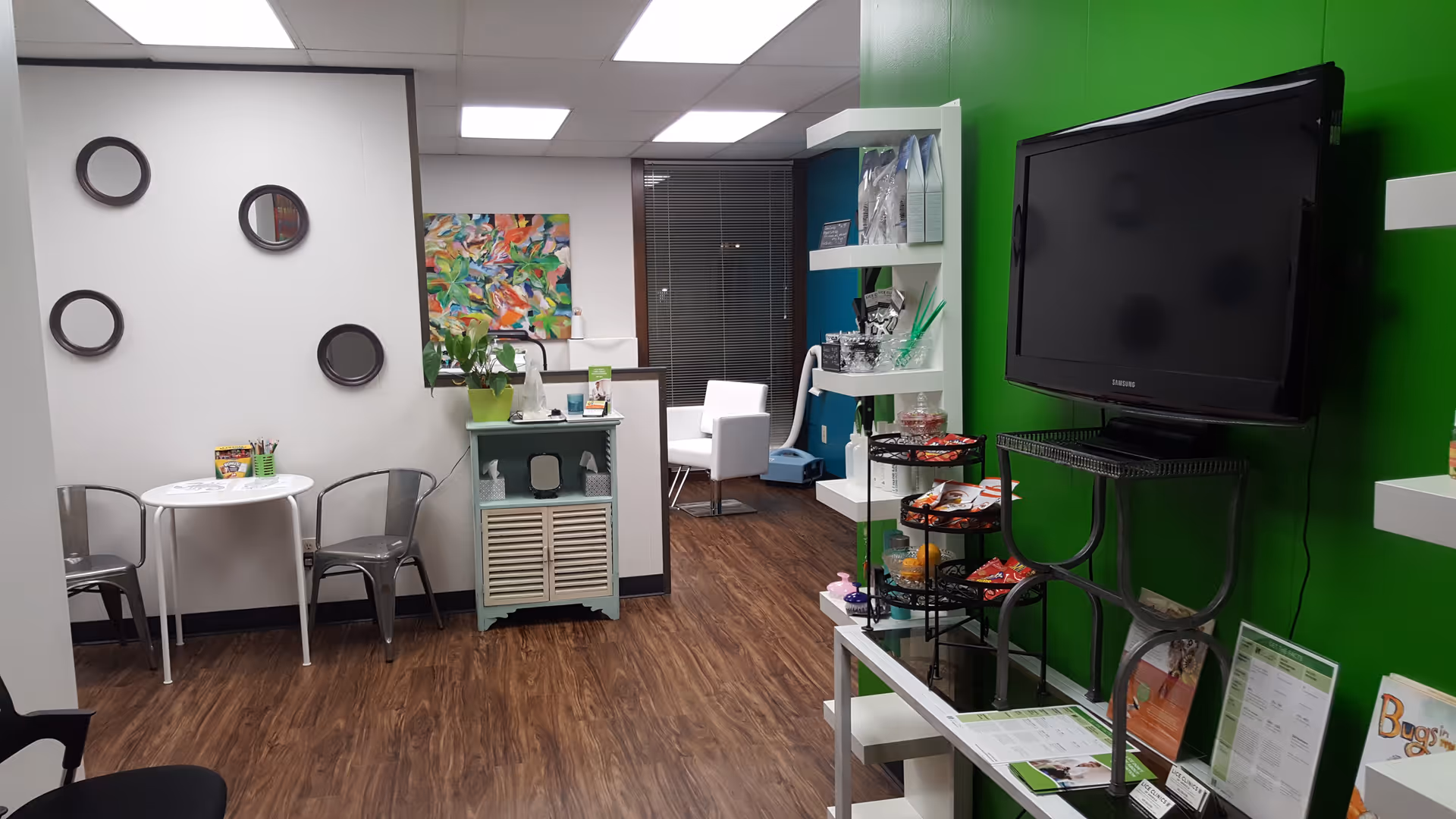 Modern facility lobby with green wall, TV, snack rack, and seating area.