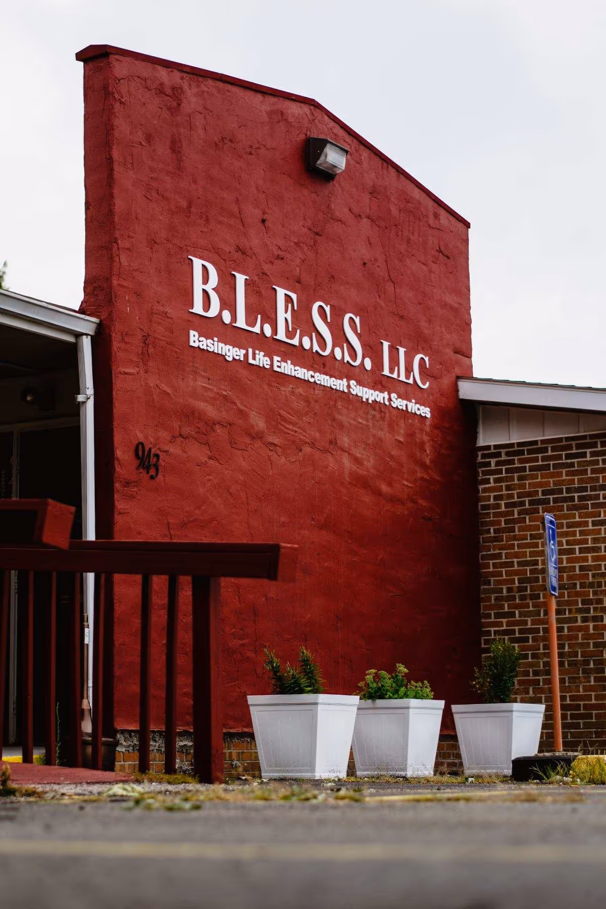 Red exterior wall with large B.L.E.S.S. LLC sign and white planters.