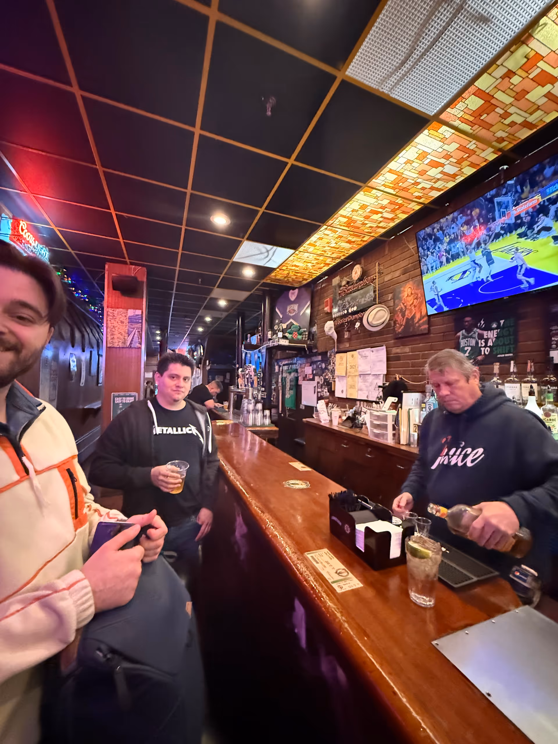 Bar counter inside a busy interior with patrons, a bartender, and a TV.