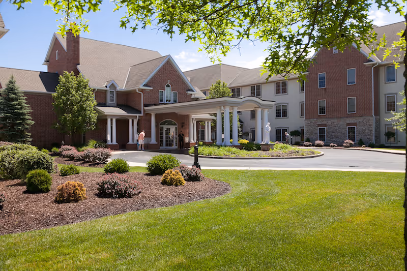 Exterior view of a senior living facility with a circular driveway and landscaped grounds.