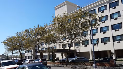 Exterior view of The Waterford on the Bay Senior Living building with trees and parked cars.