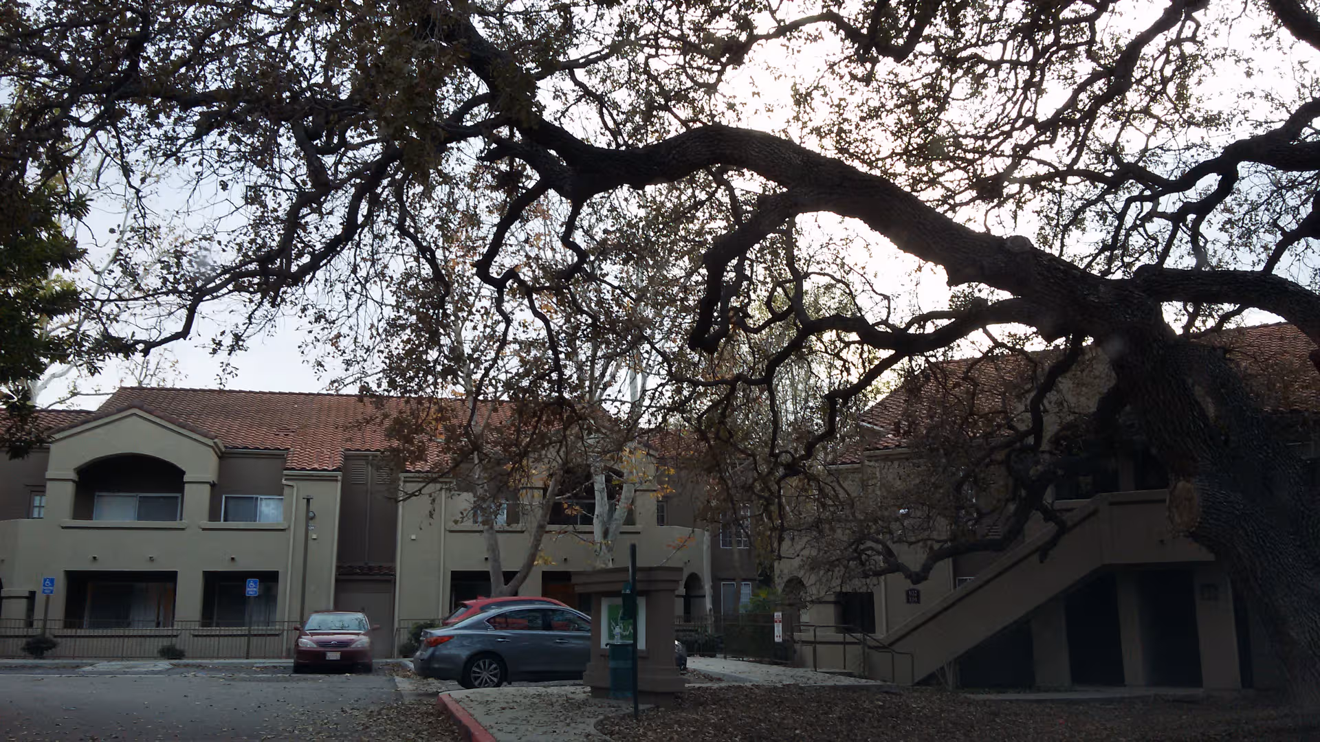 Exterior view of a tan multi-story Atria Hillcrest senior living building with parked cars and trees
