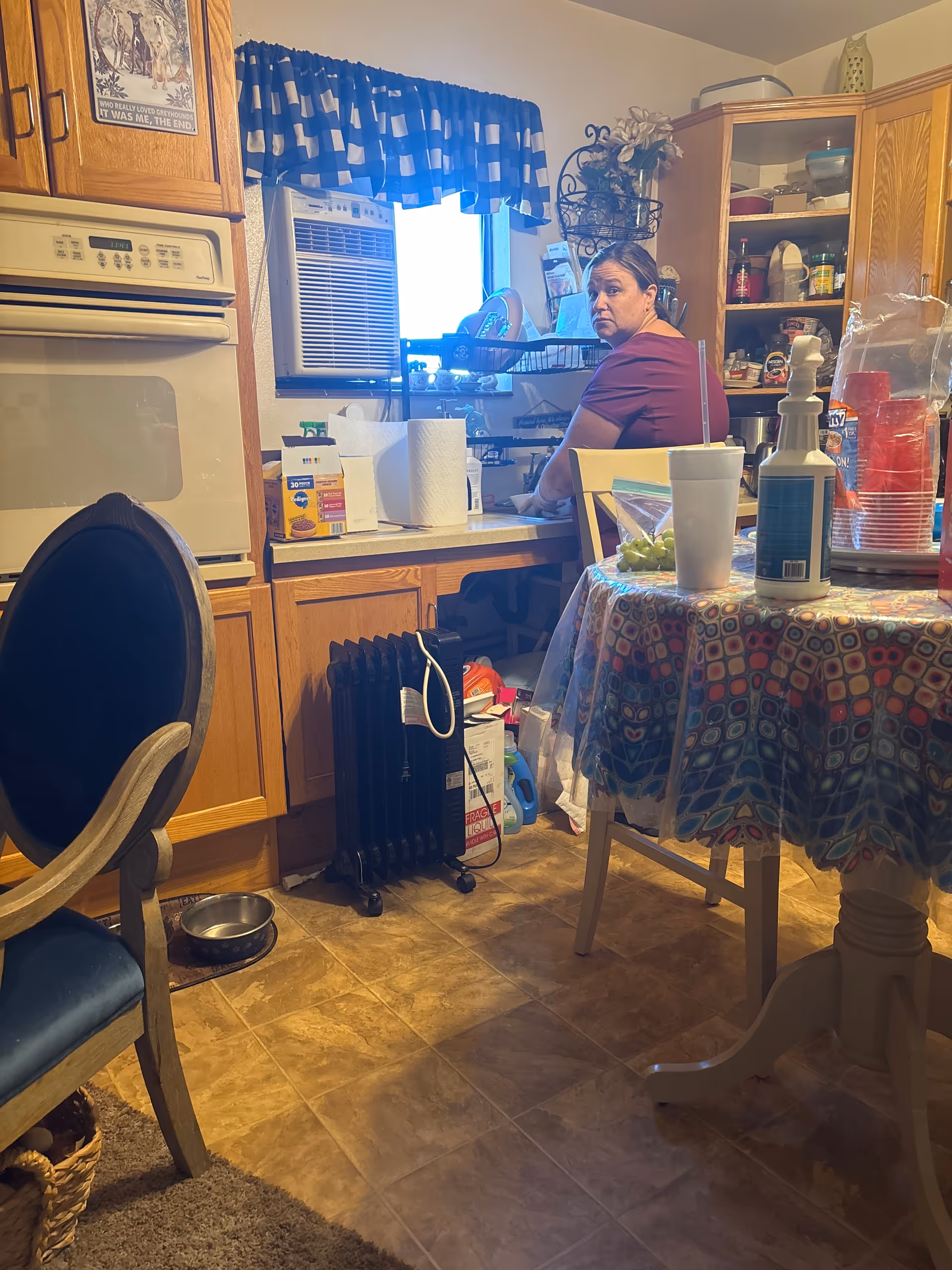 A woman stands at a kitchen sink in a cluttered, home-style senior living facility.