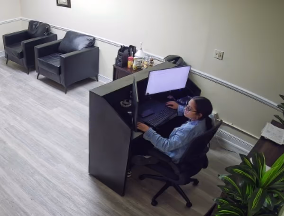 A person sits at a black desk with a computer in a lounge area.