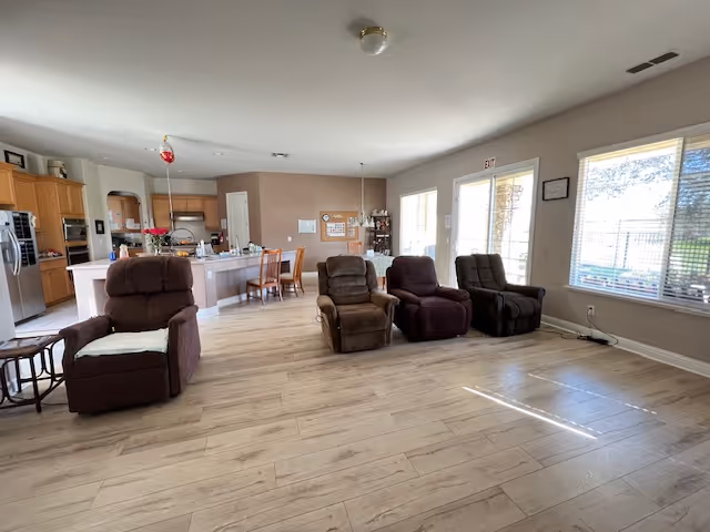 Open living area with multiple recliner chairs and a visible kitchen and dining area.