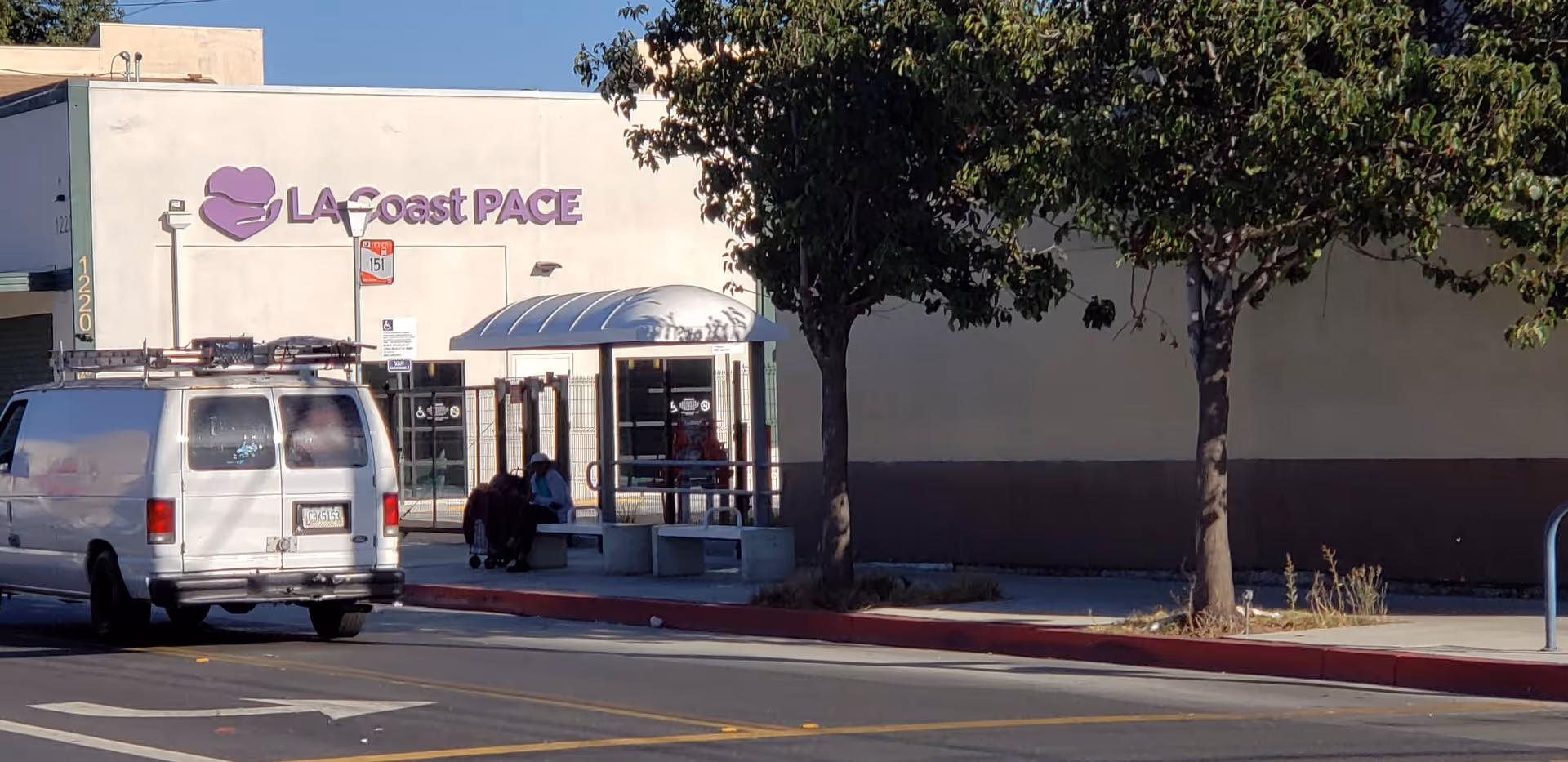 Exterior view of a building front with a purple sign, van, and people near the entrance.