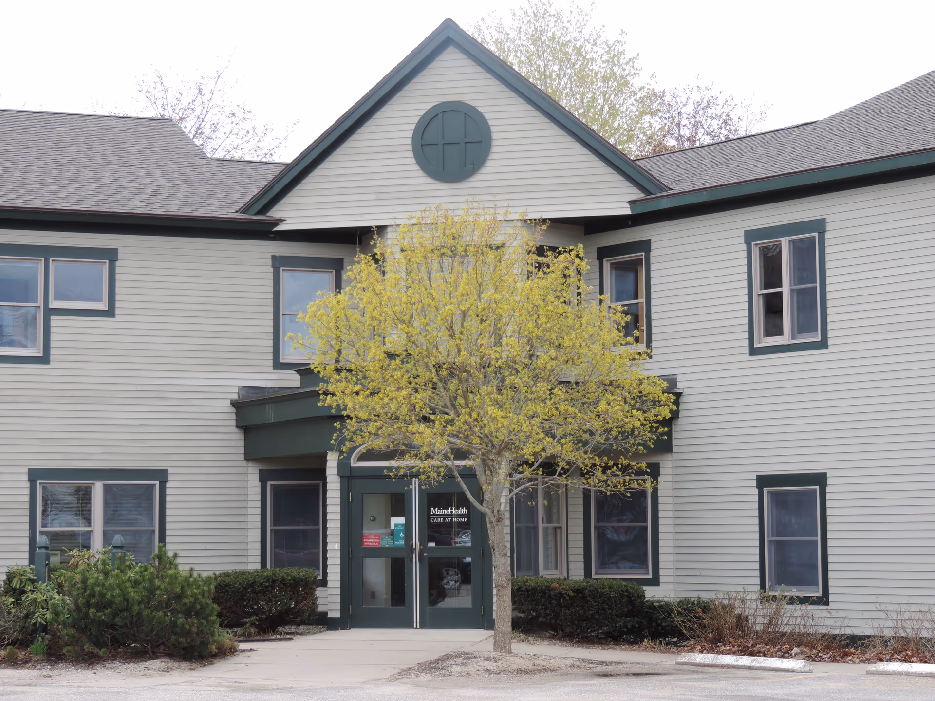 Two-story senior facility exterior with entrance doors and a tree.