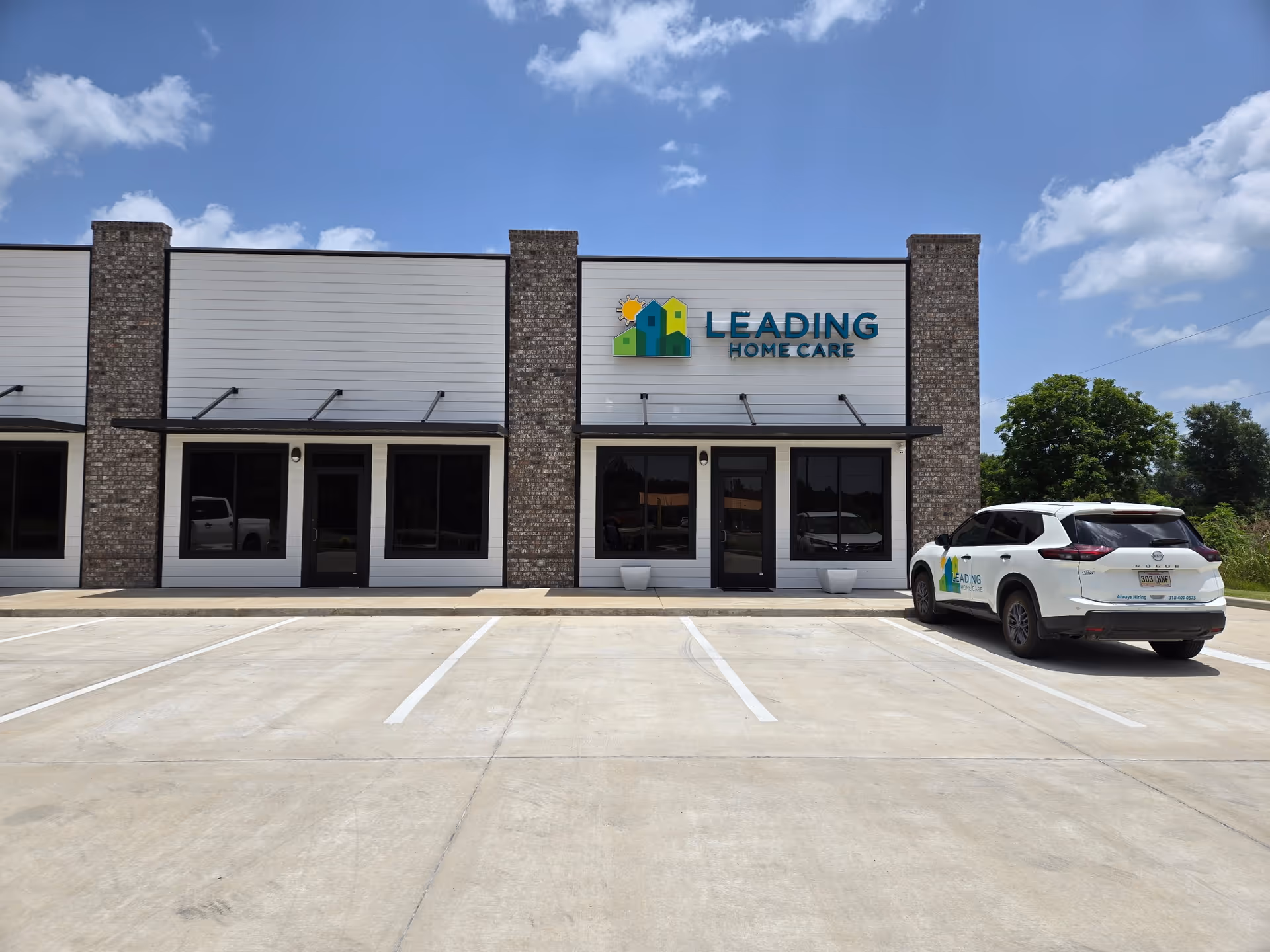 Front exterior of a brick siding facility with Leading Home Care sign and a parked SUV.