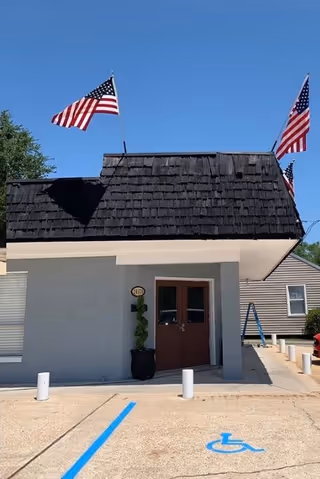 Front view of a facility entrance with two flags, a brown door, and handicap parking.