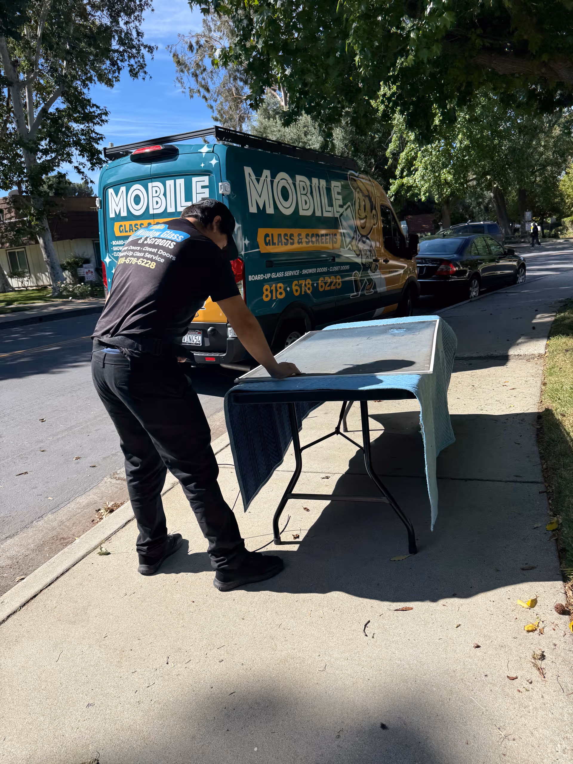 A worker stands at a table on the sidewalk beside a mobile service van.
