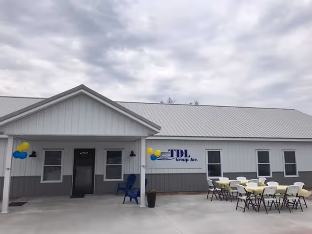 Exterior view of a light-gray senior living facility with entrance, sign, and outdoor seating.