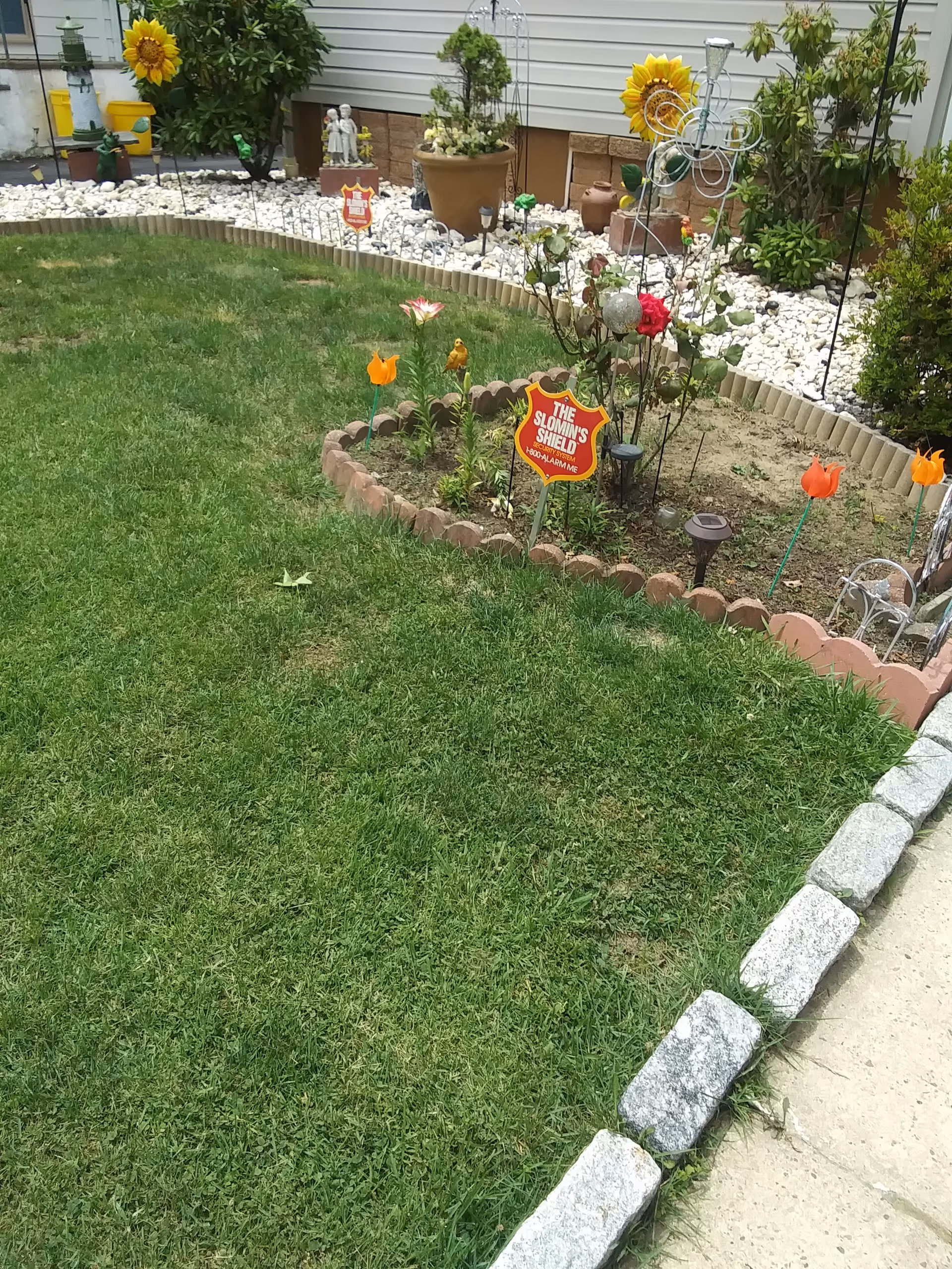 Small garden with flowers, decorative signs, and a stone border along a grassy lawn.