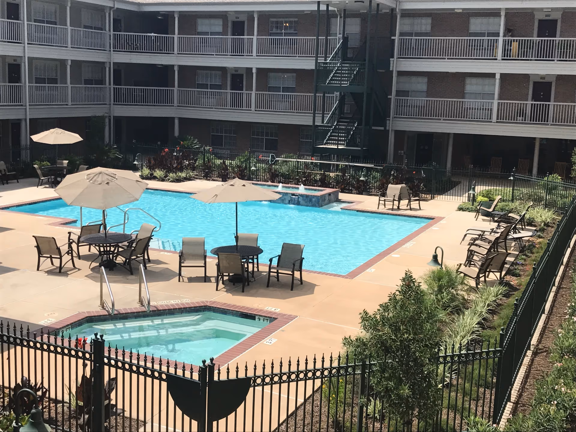 Outdoor pool area with umbrellas, seating, and a multi-story residential building.