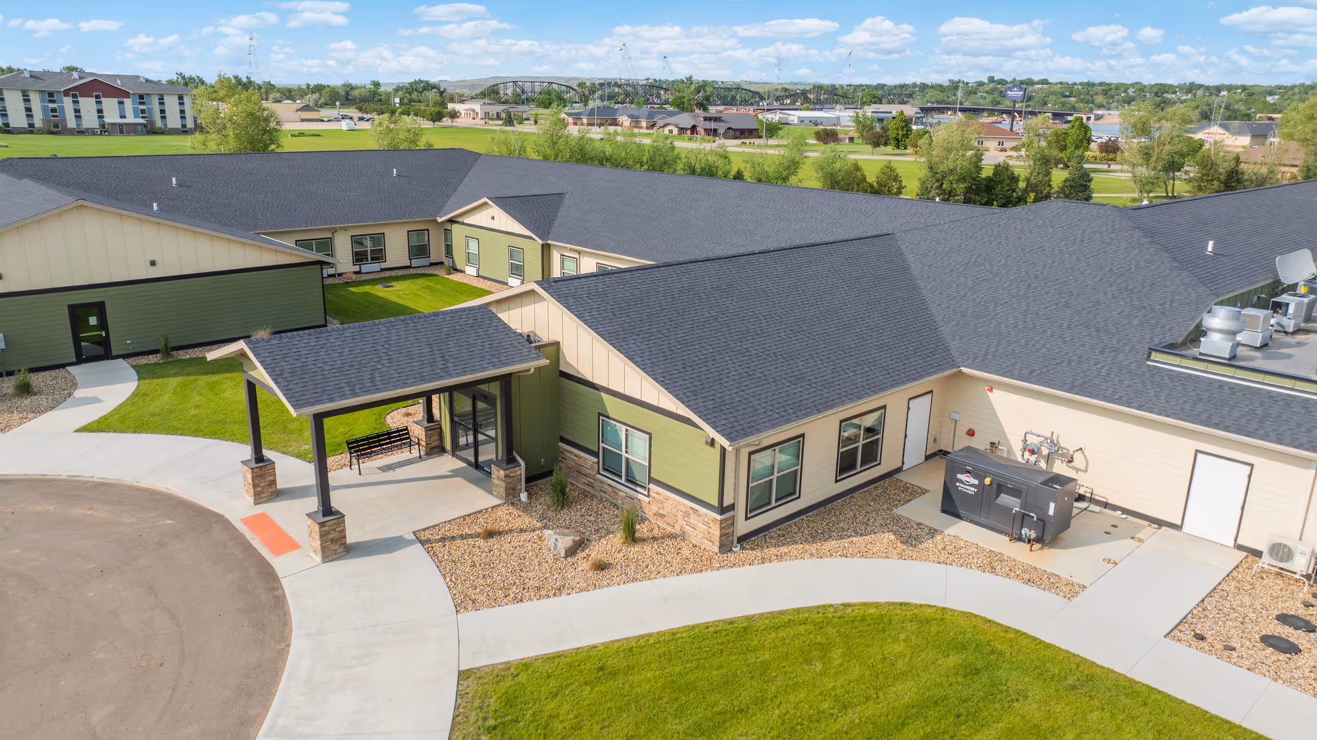 Aerial view of a modern senior living facility with green siding, dark roof, and front entrance.