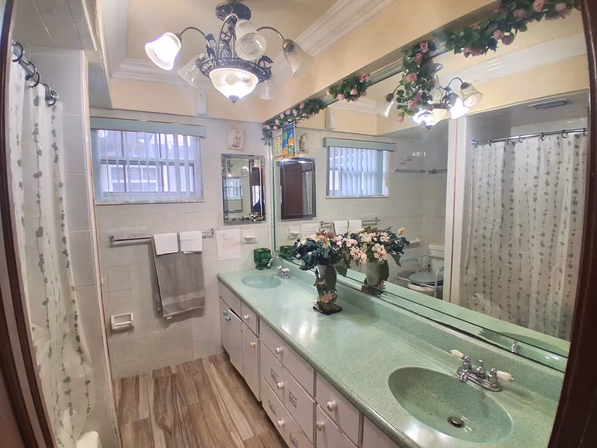 Bathroom with double sinks, large mirror, shower curtain, and decorative flowers.