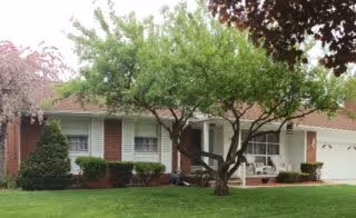 Front view of a single-story suburban house with brick siding, a lawn, small trees, and a two-car garage.