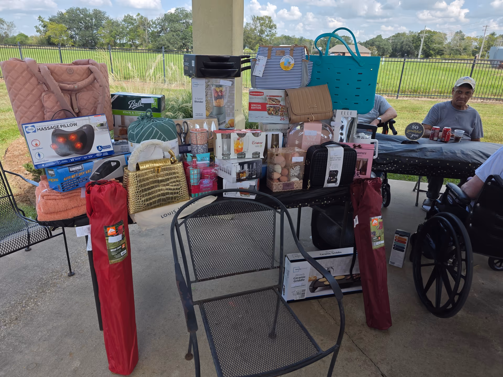 Outdoor pavilion scene with tables piled with assorted gifts and household items.