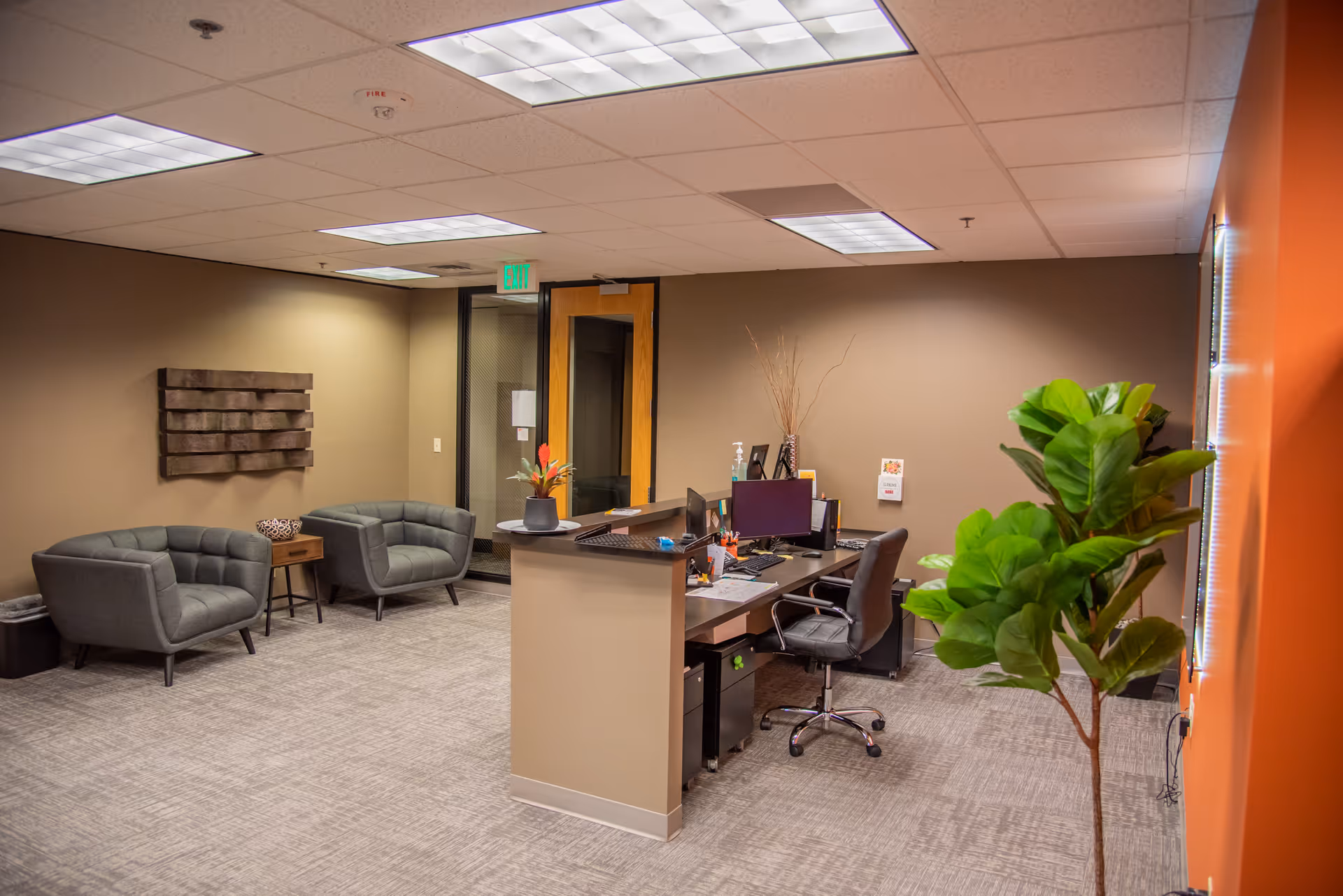 A receptionist desk in a modern lobby with seating area and plant.