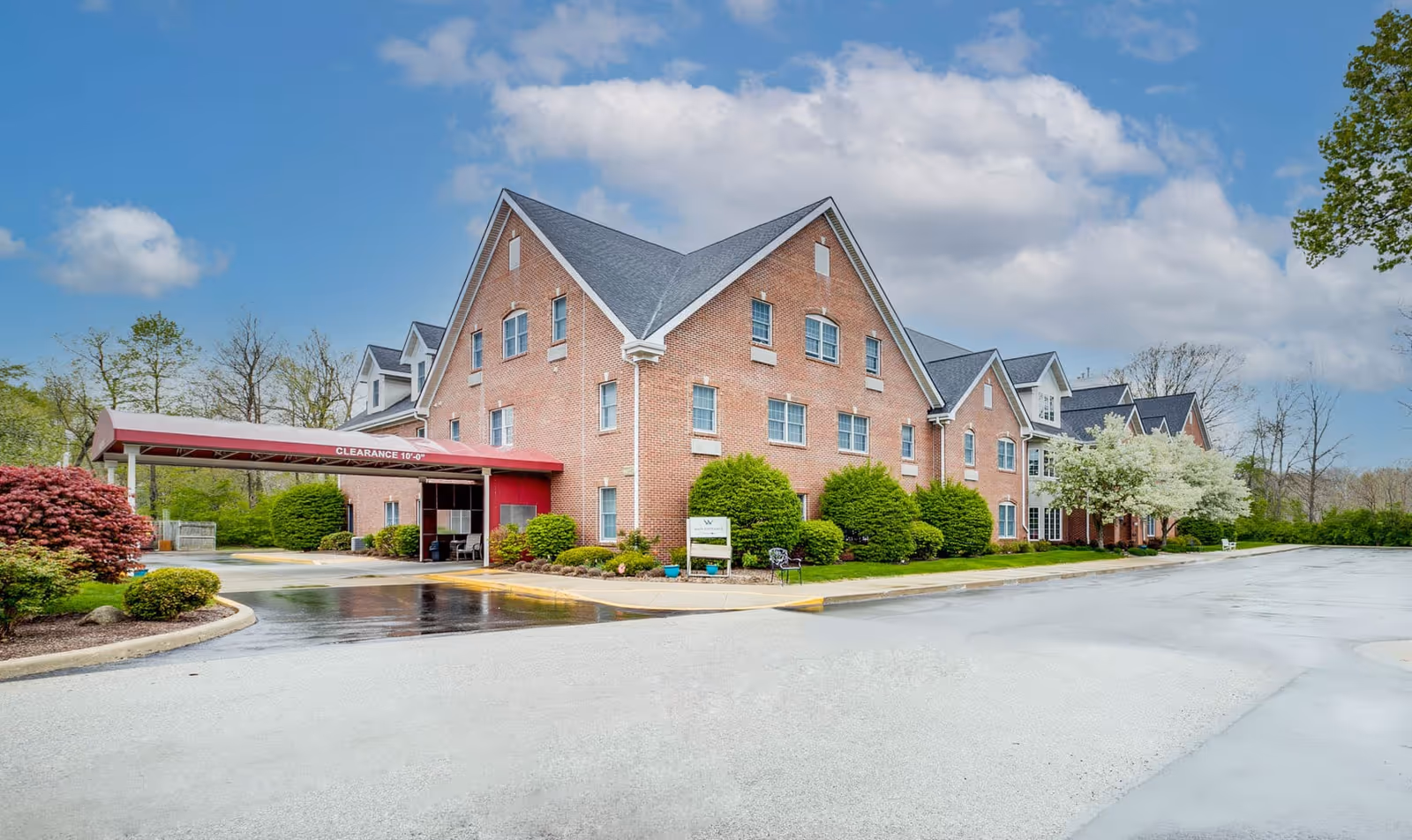 Front exterior of a brick assisted living building with a covered entrance canopy and landscaped grounds.