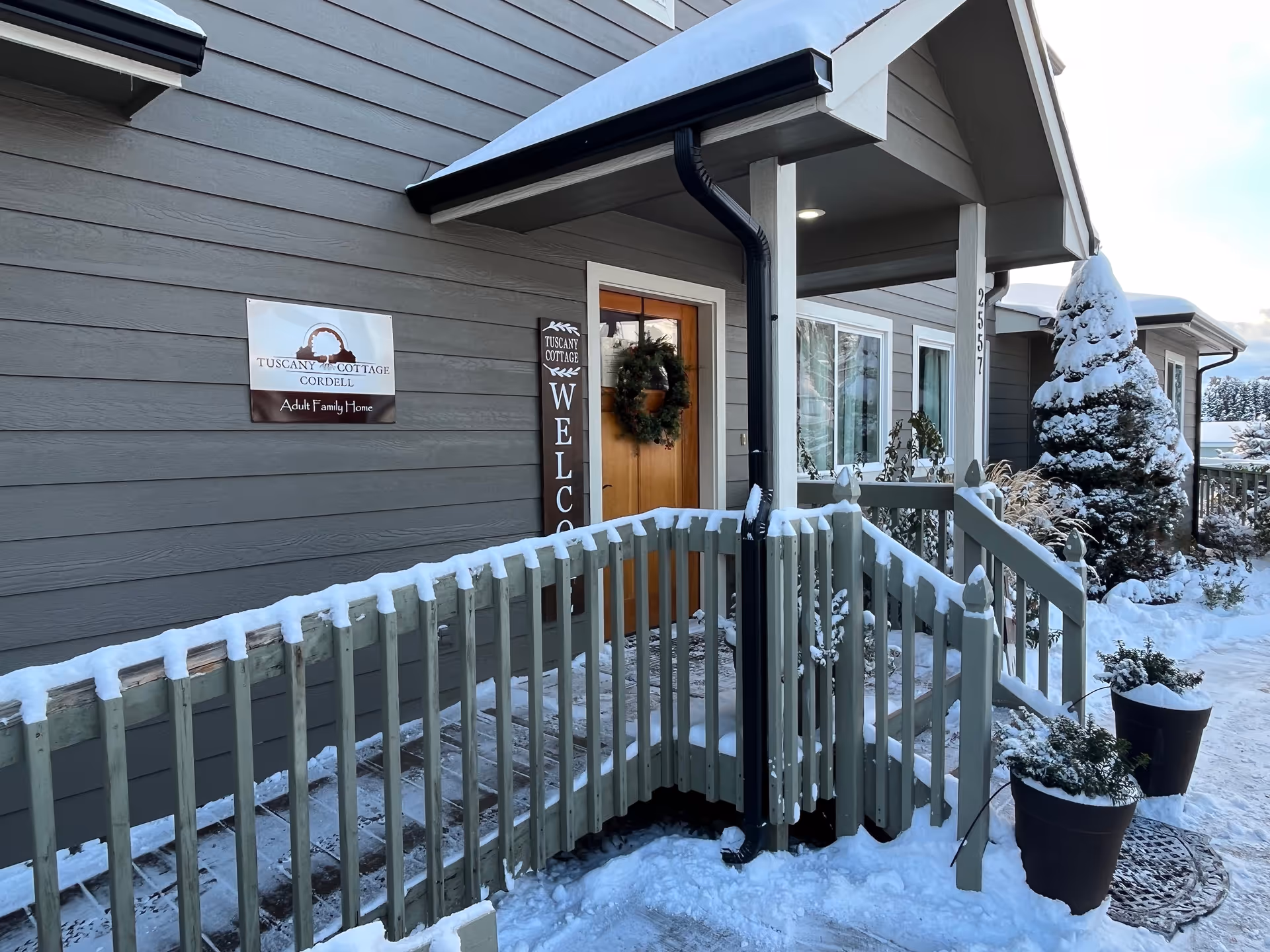 Snowy exterior of Tuscany Cottage Cordell Adult Family Home with entrance wreath and railing
